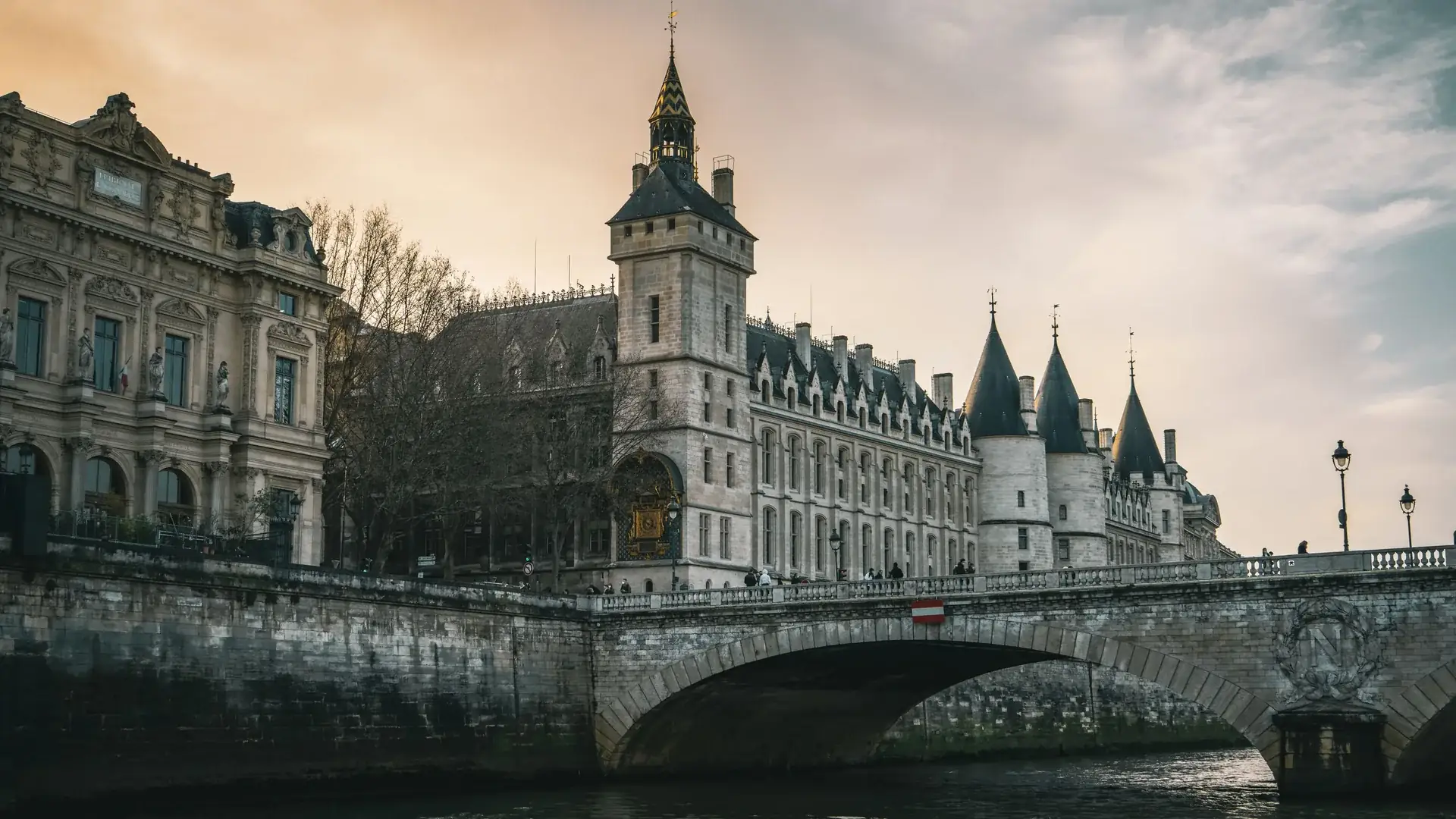 Věžička s hodinami a kuželové věže Conciergerie nad Seinou za soumraku, pohled z řeky pod Pont au Change