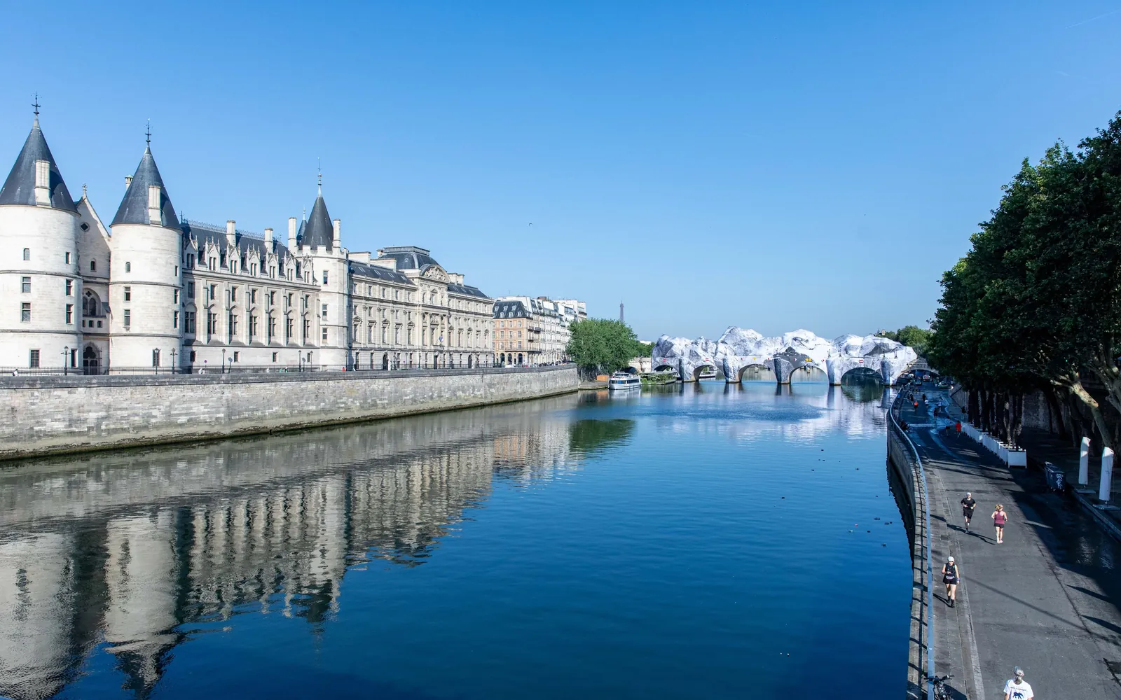The Conciergerie's white towers and long riverfront reflected in the Seine under a clear sky
